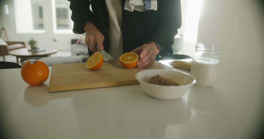 A person standing by a counter cutting an orange with a knife on a cutting board