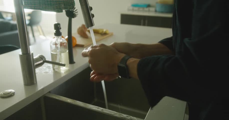 A person washes their hands at a kitchen sink