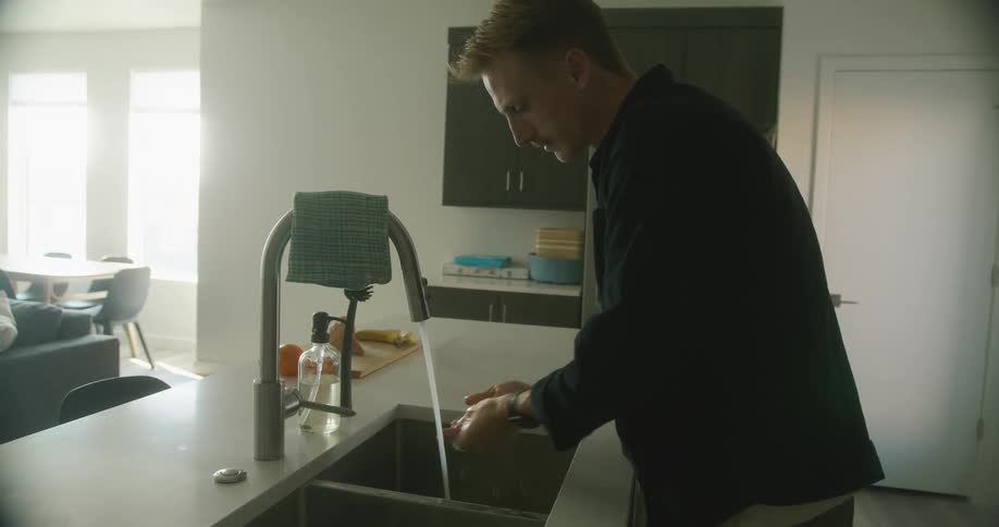 A man washing his hands at a kitchen sink at home