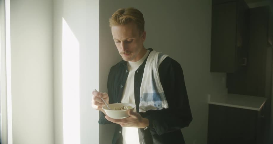 A man in a room eating with a spoon and bowl