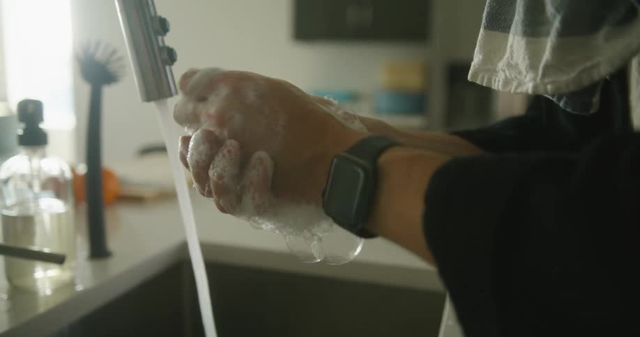A person in a room washing their hands with soap over a sink