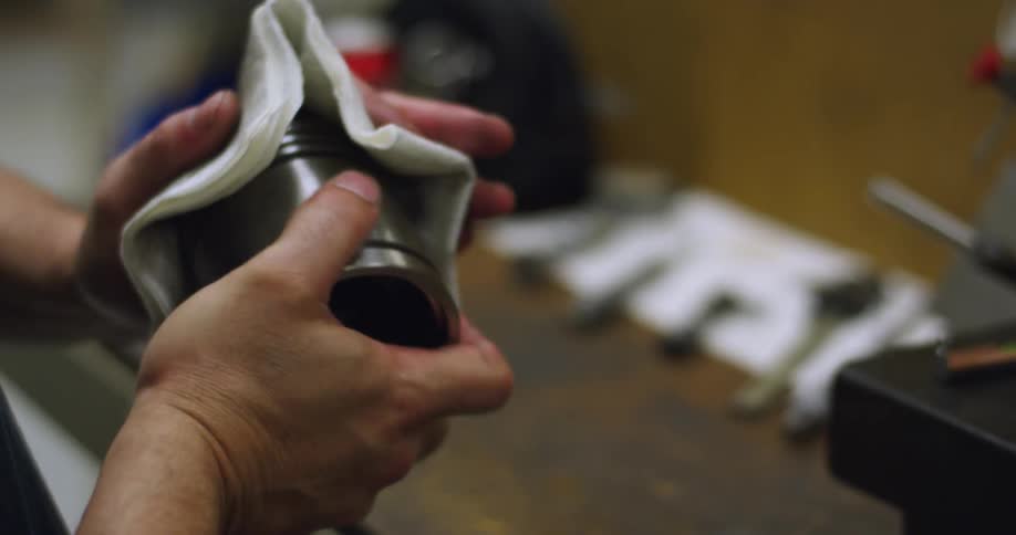 A man cleaning a metal part while standing at a workbench