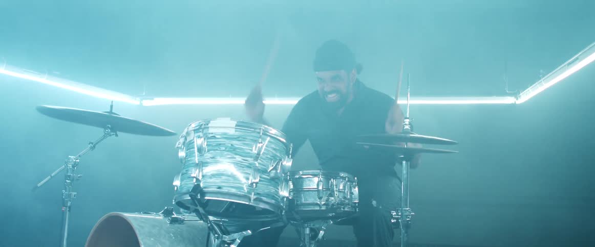 Male drummer with a headband and a beard plays drums in a foggy dim lit room
