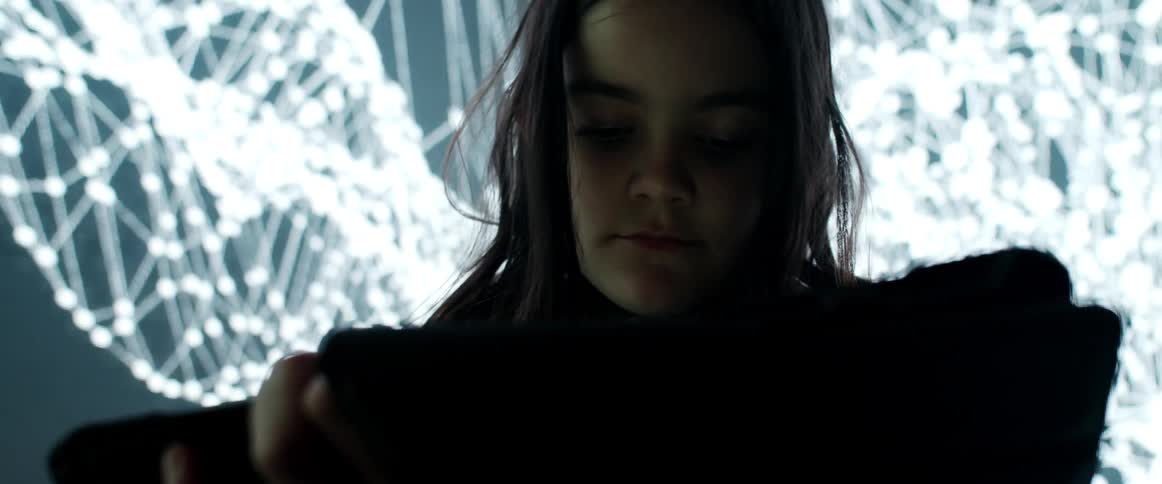 A girl using a tablet in a room with a screen in the background