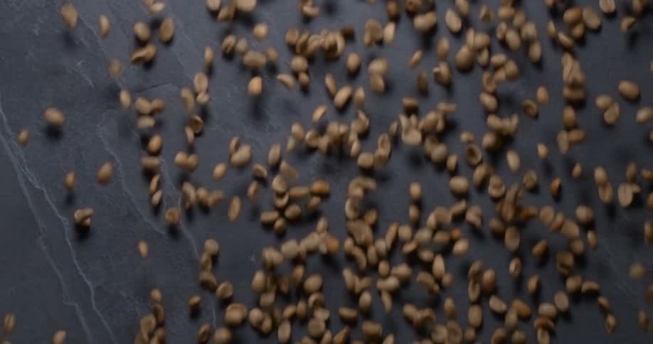 Light brown coffee beans fall and flutter against a gray stone background