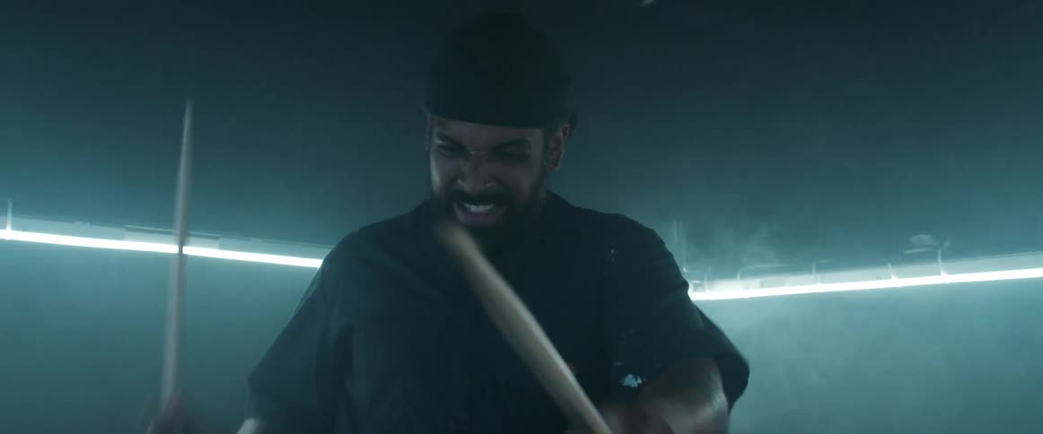 Man with a black beanie and a beard plays the drums in a room with lights