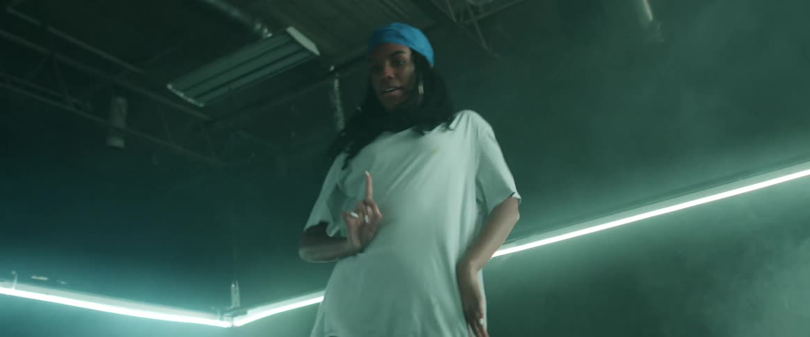 Woman with braids hoop earrings and a loose white t shirt dances in a dark room