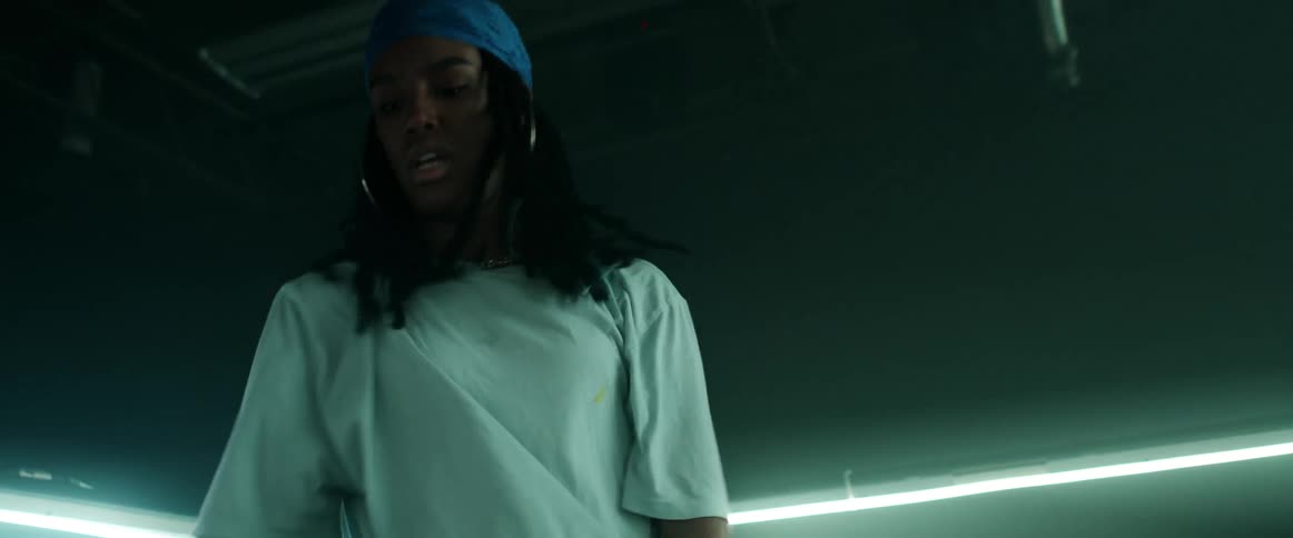 Woman with a blue headband braids hoop earrings and a white loose t shirt dances in a dark room with lights
