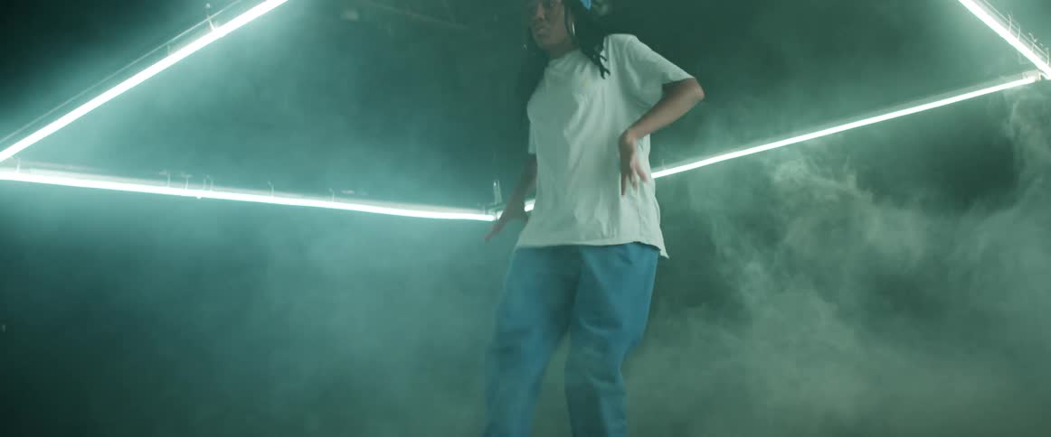 A young woman dances under a light fixture in a smoky room