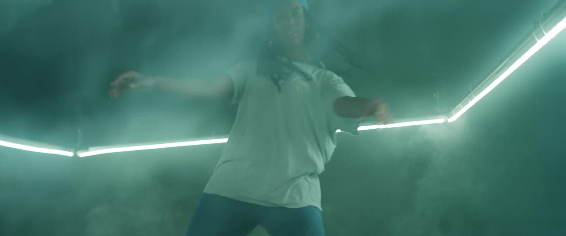 Woman dances in foggy room dimly lit by neon light lined wall