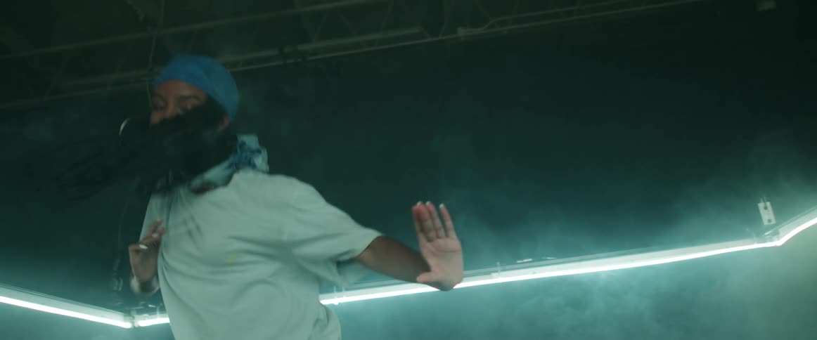 A young woman dancers under a rectangular light fixture in a smoky room
