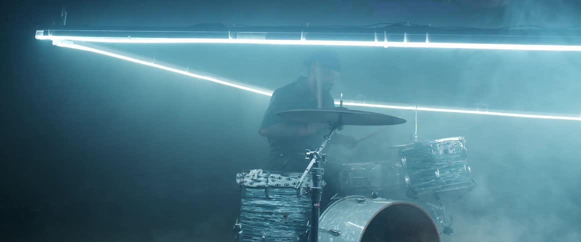 Drummer playing a drum set surrounded by a ring of lights inside a room filled with white smoke