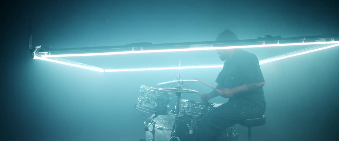 A man with a hat in a room playing drums with drumsticks