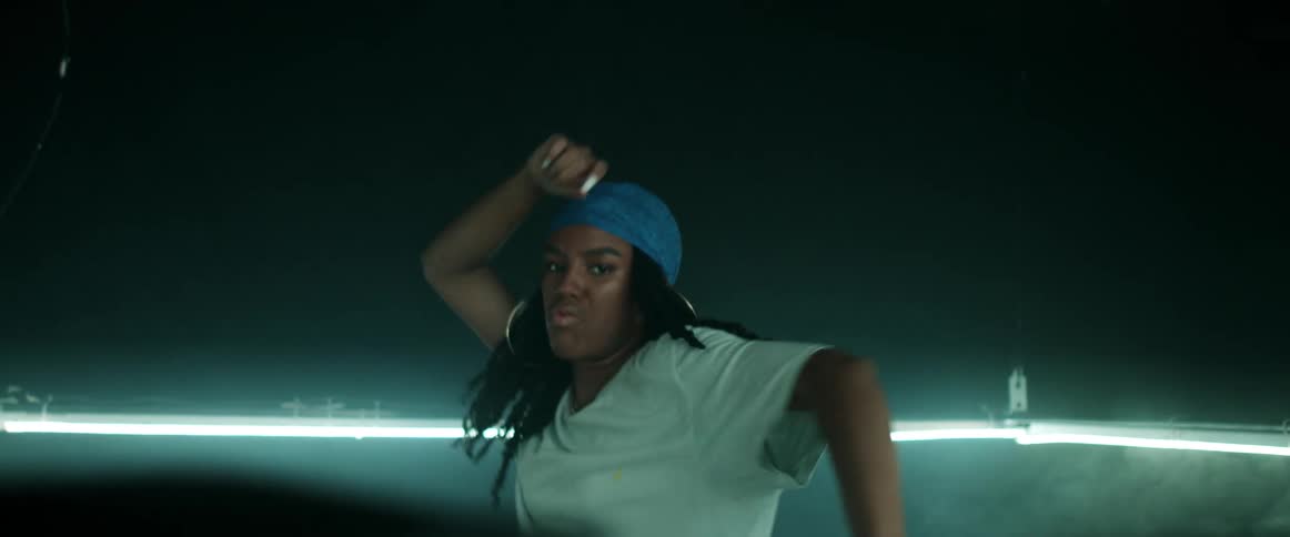 A woman dances in the center of a rectangular light fixture in a smoky room