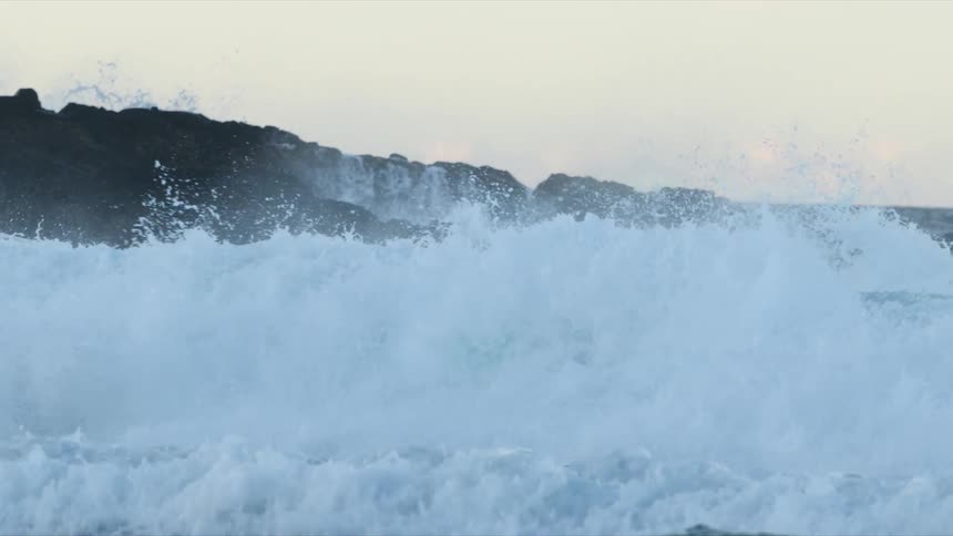 Waves of water crashing on a rocky shore with the sky and clouds in the background