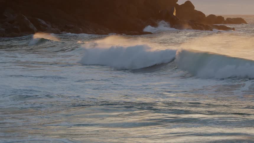 Wave rolls in splashing as the sun is setting in the distance