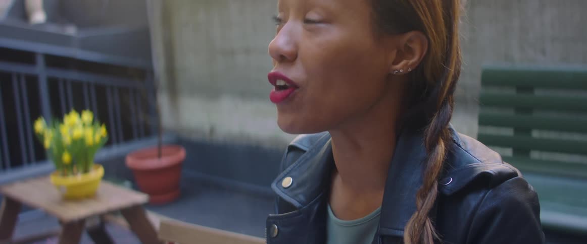 An asian woman sitting in an outdoor patio area is listening and talking to another person