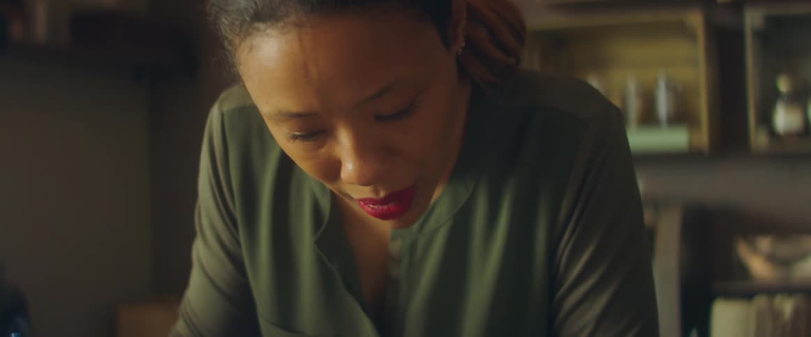 A woman in a room holding a pen with a wall and shelves in the background
