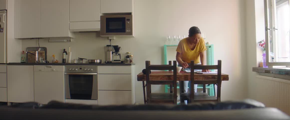 A woman in a kitchen drinking from a mug with a stove and a sink in the background