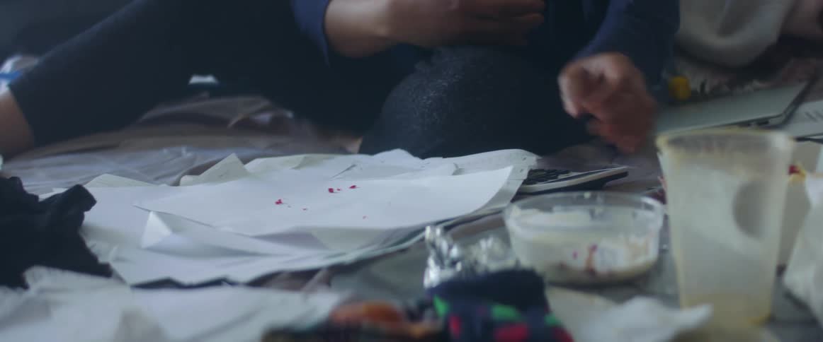 Woman sitting on bed eating and working organizes papers cleans crumbs and shuts laptop