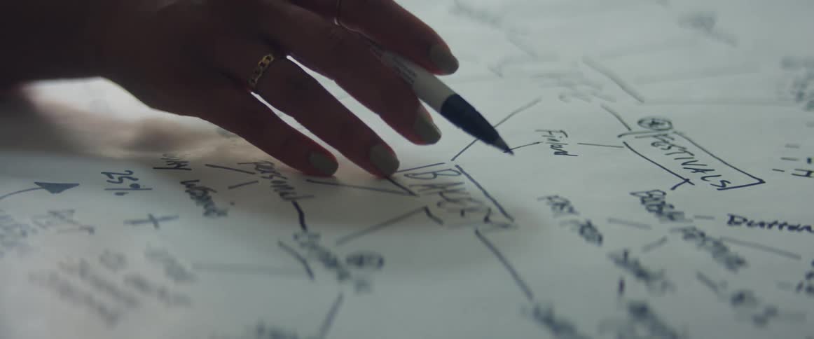 A person explaningn a diagram drawed on a sheet of paper over a desk