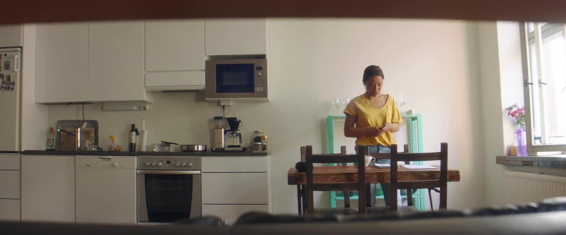 A woman in a kitchen using a smart phone with a stove and a sink in the background