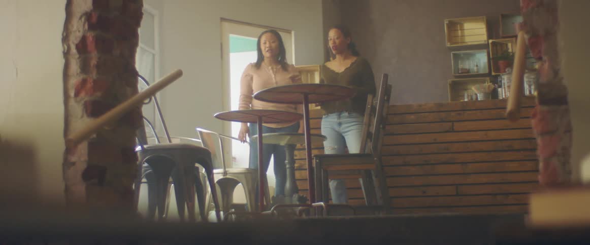 A woman gestures around a room with her arms while speaking with another woman as they stand together