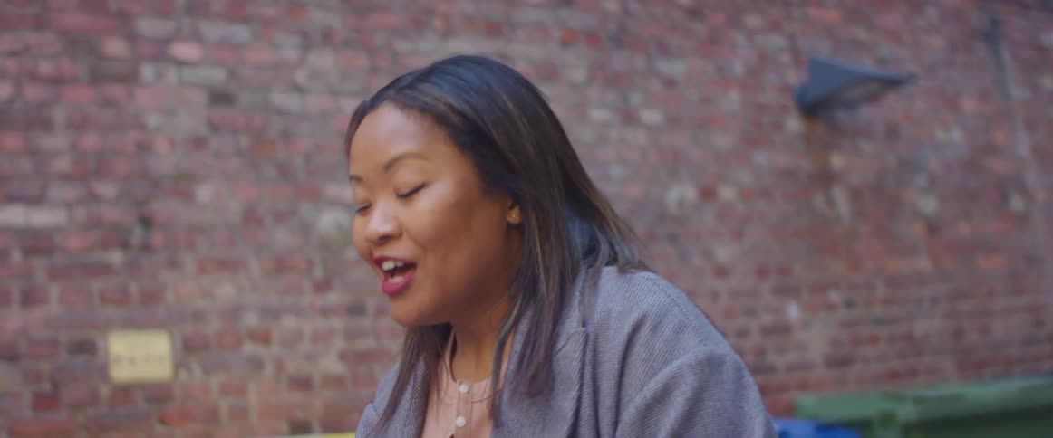 A woman stands outside a city building talking to another woman