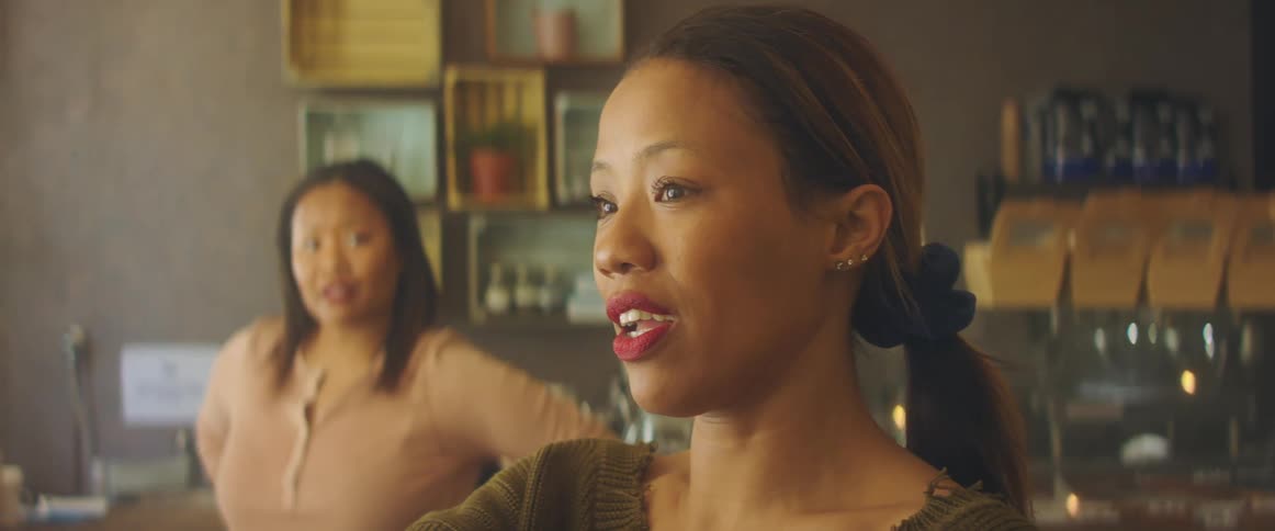 A woman smiles proudly as she points and talks to a barista behind the counter
