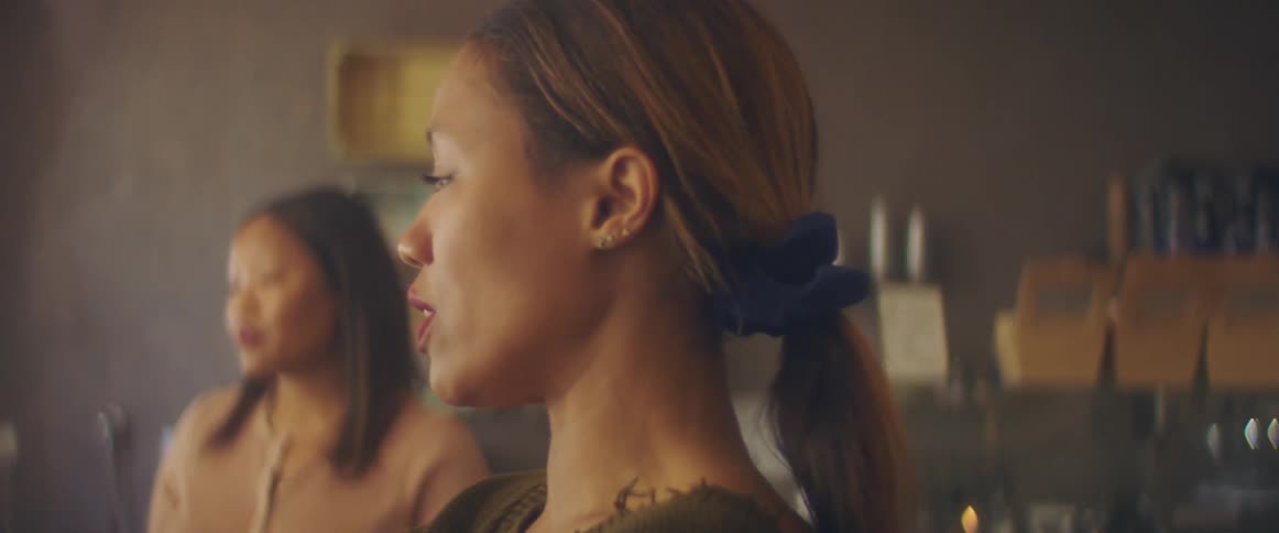 Two women in a room talking with a wall with shelves and containers in the background