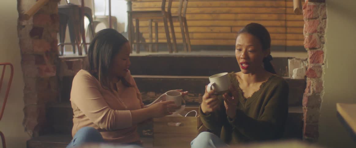 Two women unpack coffee cups sitting on steps in between rooms of business