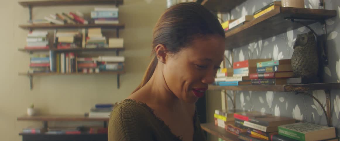 A woman in a room with books bookshelves and a wall in the background