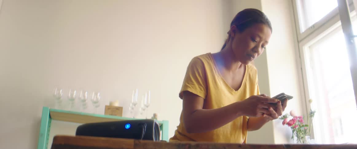 A woman in a room using a smart phone with a wall and window in the background