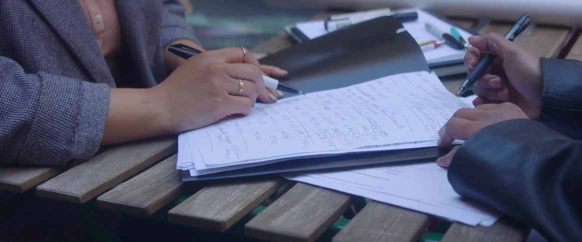 Two women sit at wooden table making changes to paperwork