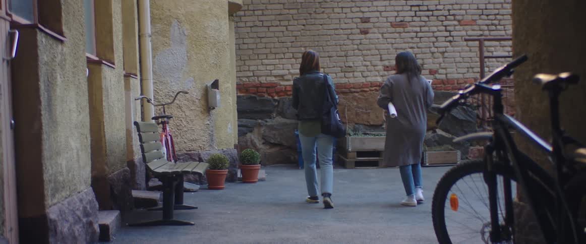 Two teenage girls walk towards an apartment building and one unlocks the door