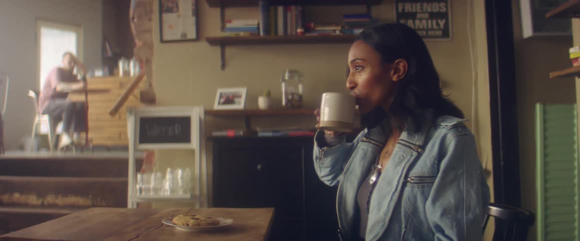 A woman smiles and puts her book down as a man delivers her coffee and cookie in a cafe