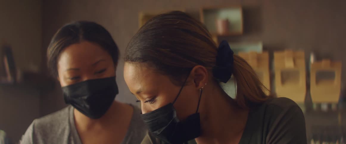 A pair of young women in medical masks work together indoors during the day