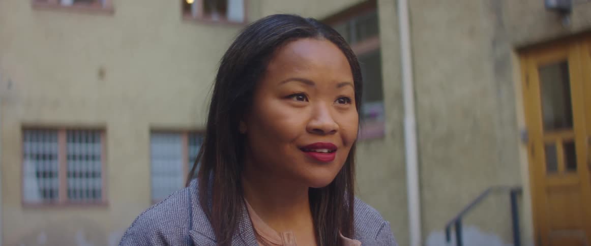 An asian woman stands outside a building and listens as someone talks to her