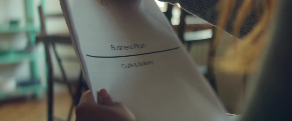 A female holds a document that is labeled as a business plan for a cafe and bakery