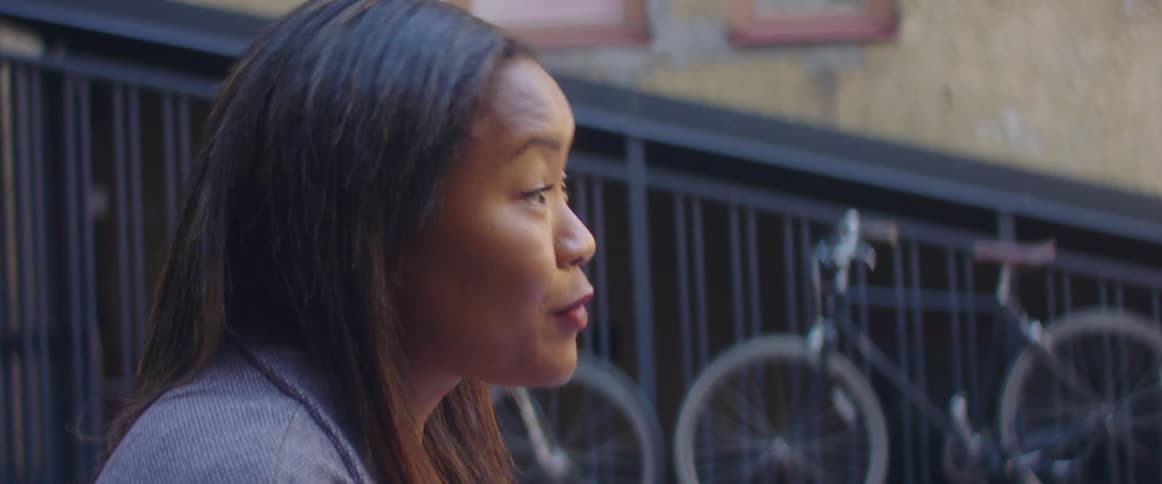A woman is sitting outdoors by a fence