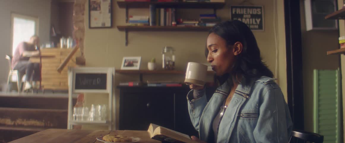 A woman reads a book and drinks coffee while sitting in a cafe