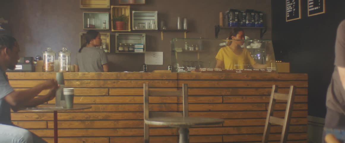 Two women behind a counter in a caf with a wall and shelves in the background