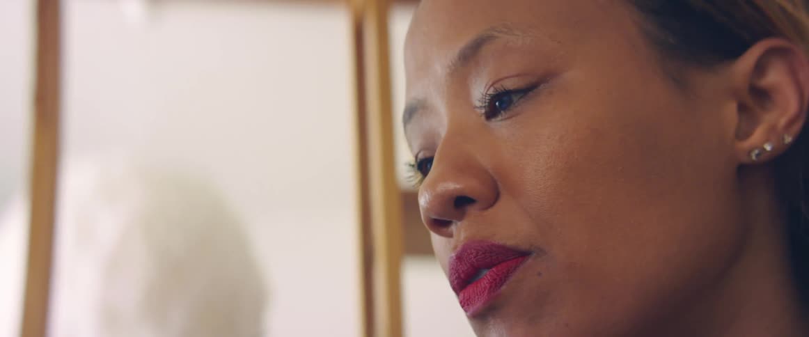 A woman in a room with earrings with a wall and a shelf in the background