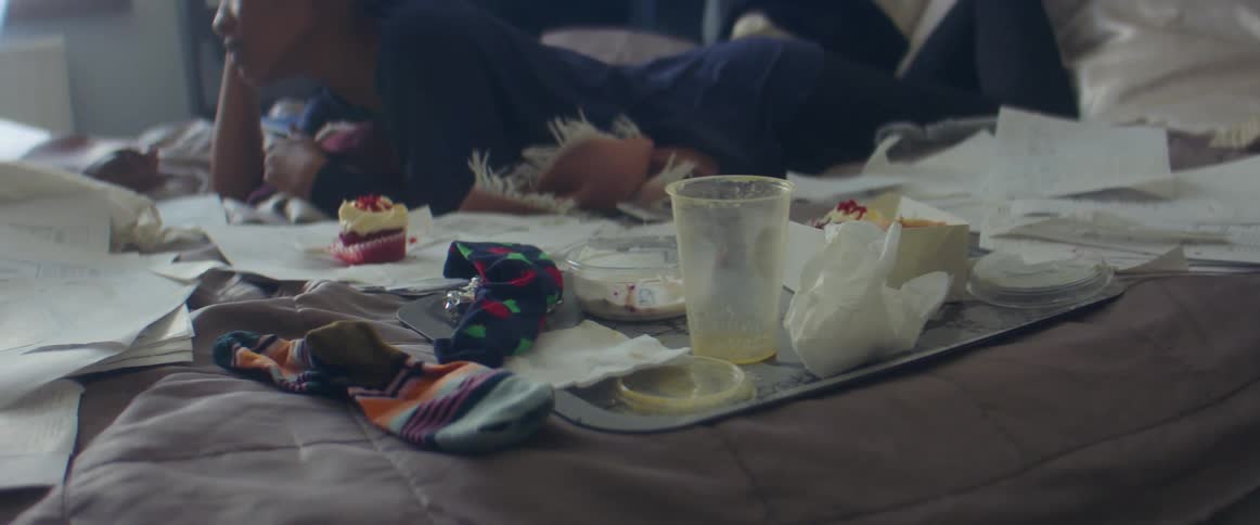 A woman lays on a bed with a dirty empty food tray beside her