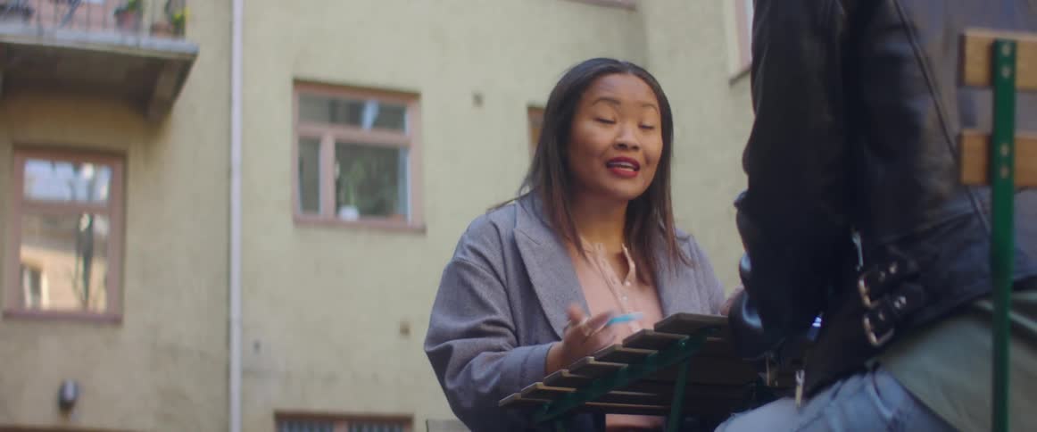 Woman sitting on a table outside a building talking to a friend