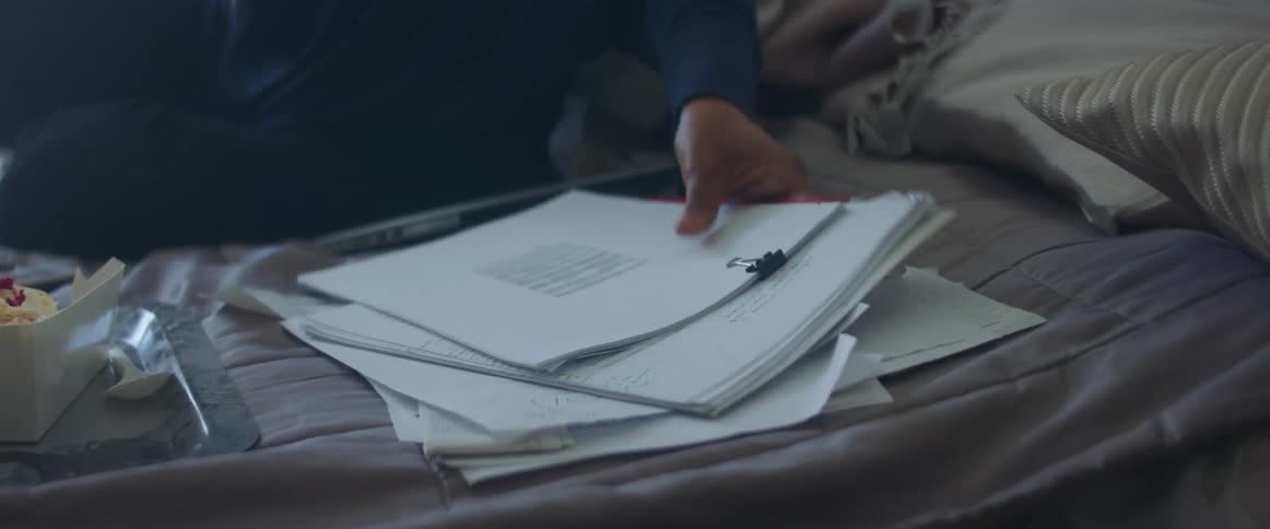 A woman sits on a bed and sorts through papers