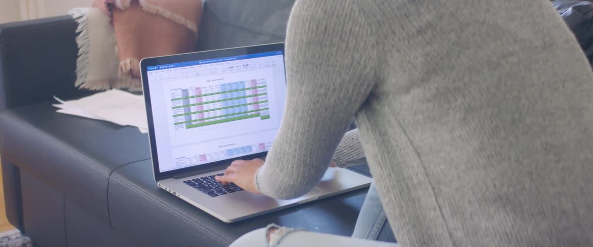 A woman types on a laptop laying beside her on a leather sofa