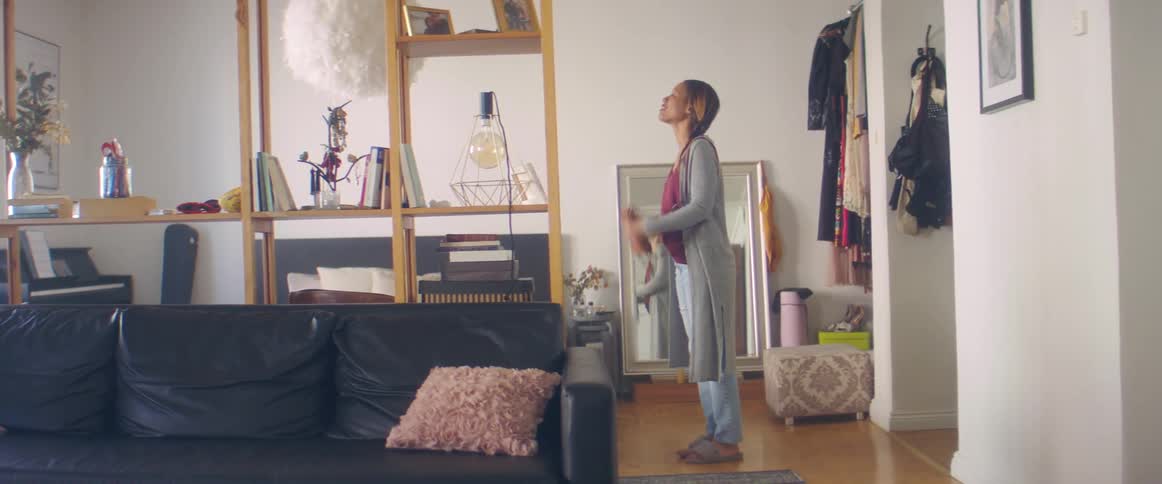 A woman walks into the living area of a home and excitedly flops on the bed