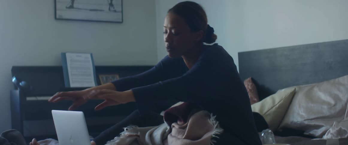 A woman looking frustrated while sitting atop her bed closes her laptop