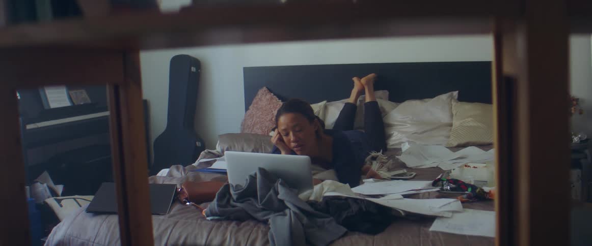 A woman is laying on her bed and looking at a laptop